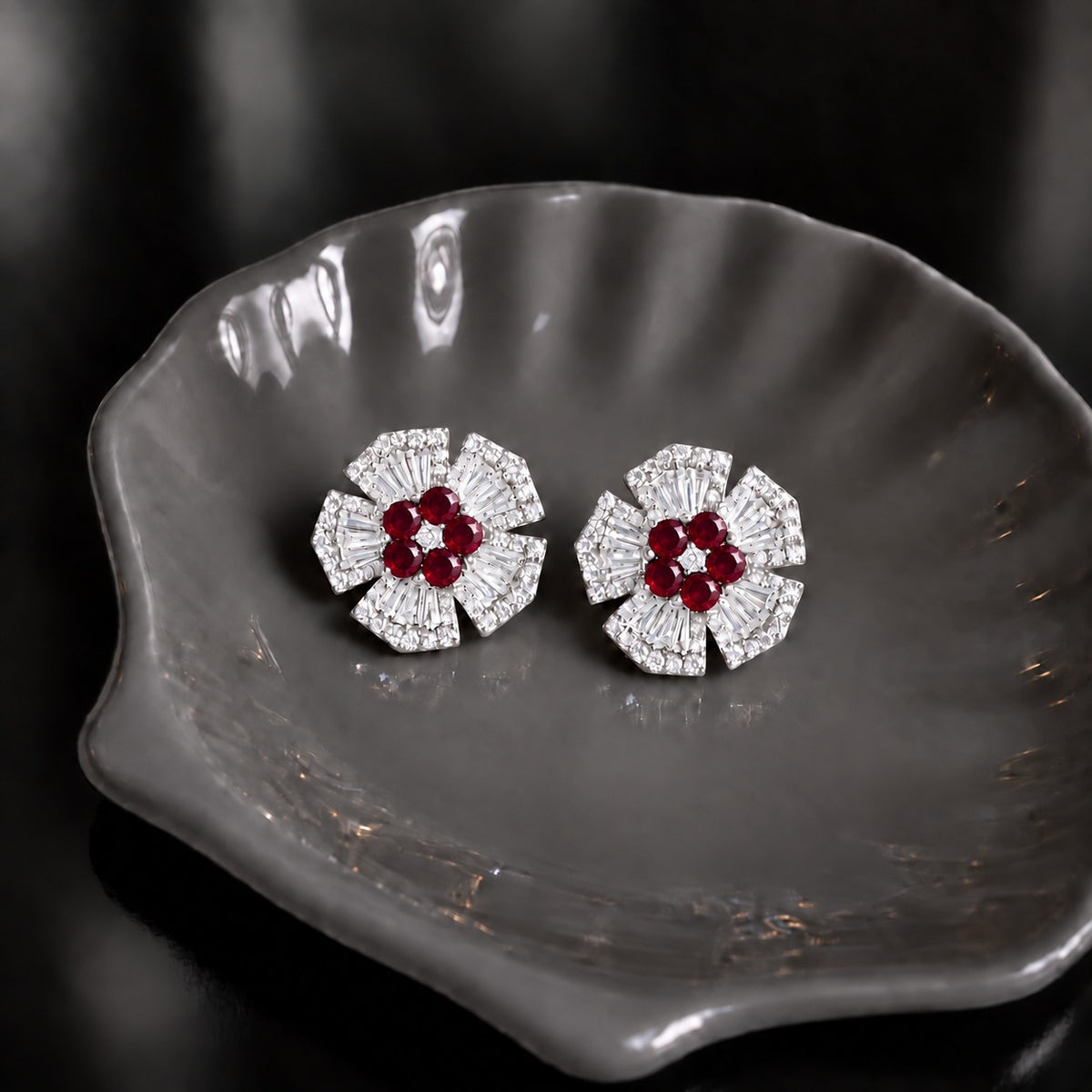 Radiant Crest Stud earrings with clear baguette zircon detailing and red centre stones, displayed on a smoky grey dish.