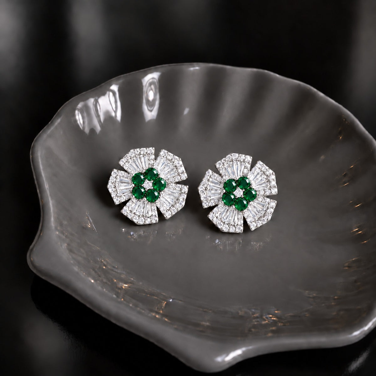 Radiant Crest Stud earrings with clear baguette zircon detailing and green centre stones, displayed on a smoky grey dish.