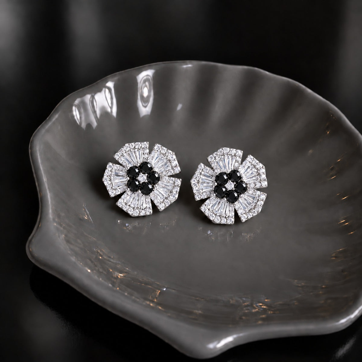 Radiant Crest Stud earrings with clear baguette zircon detailing and black centre stones, displayed on a smoky grey dish.