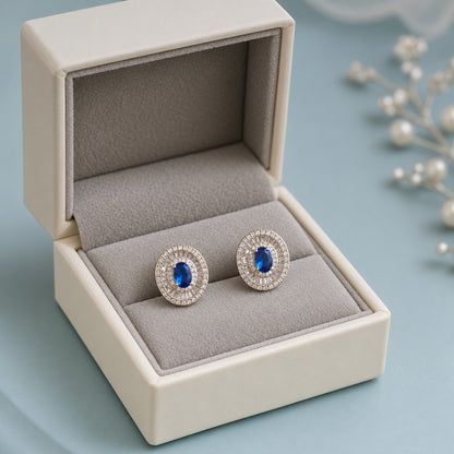 Crownline Oval Studs featuring a faceted oval blue centre crystal framed by baguette-cut and round clear zircon stones in a polished silver-tone setting.