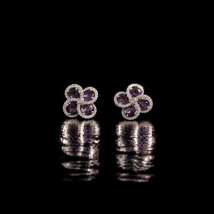 Quadra Halo Stud Earrings with four faceted  purple stones, clear zircon borders and silver-tone setting displayed on a glossy black reflective surface.