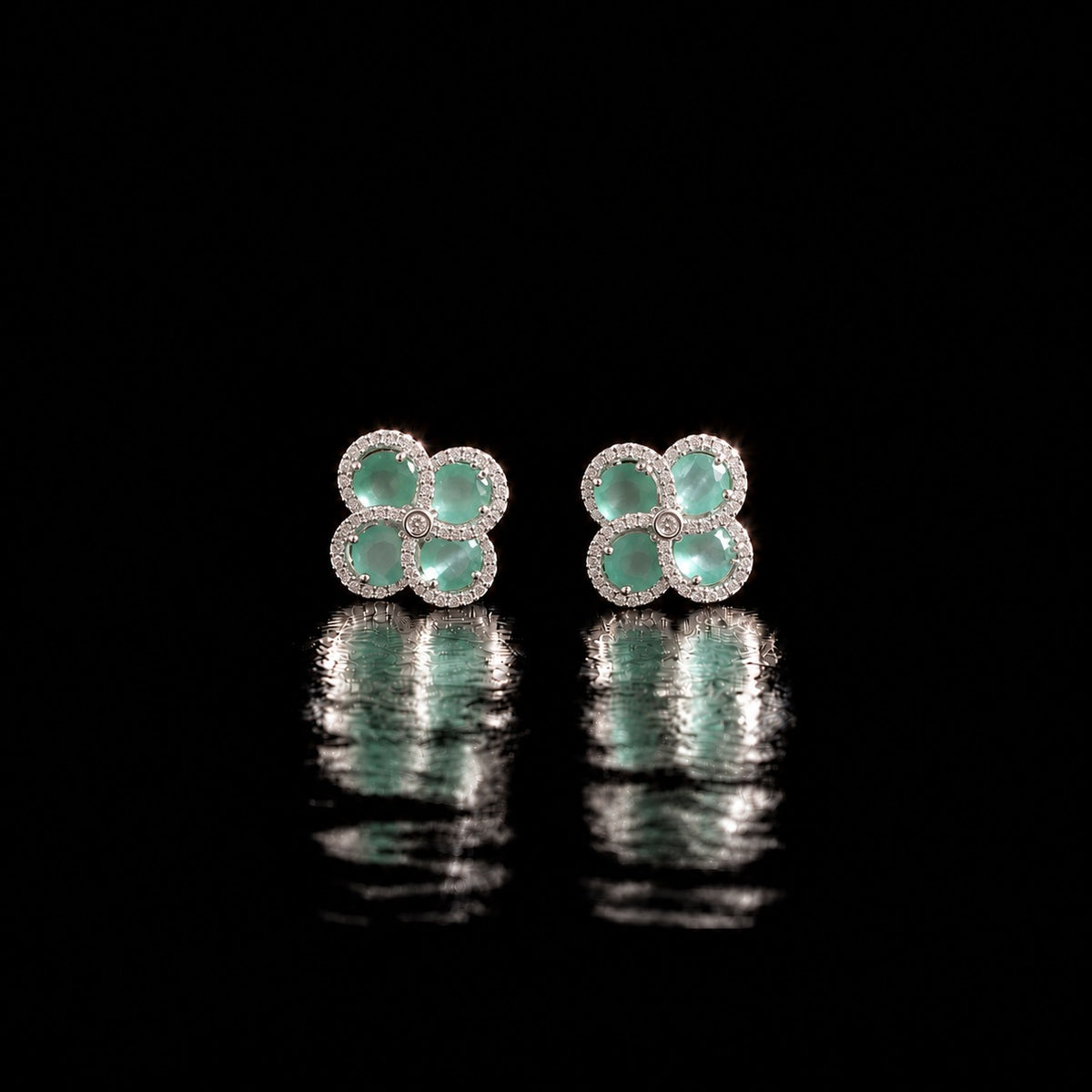 Quadra Halo Stud Earrings with four faceted mint aqua stones, clear zircon borders and silver-tone setting displayed on a glossy black reflective surface