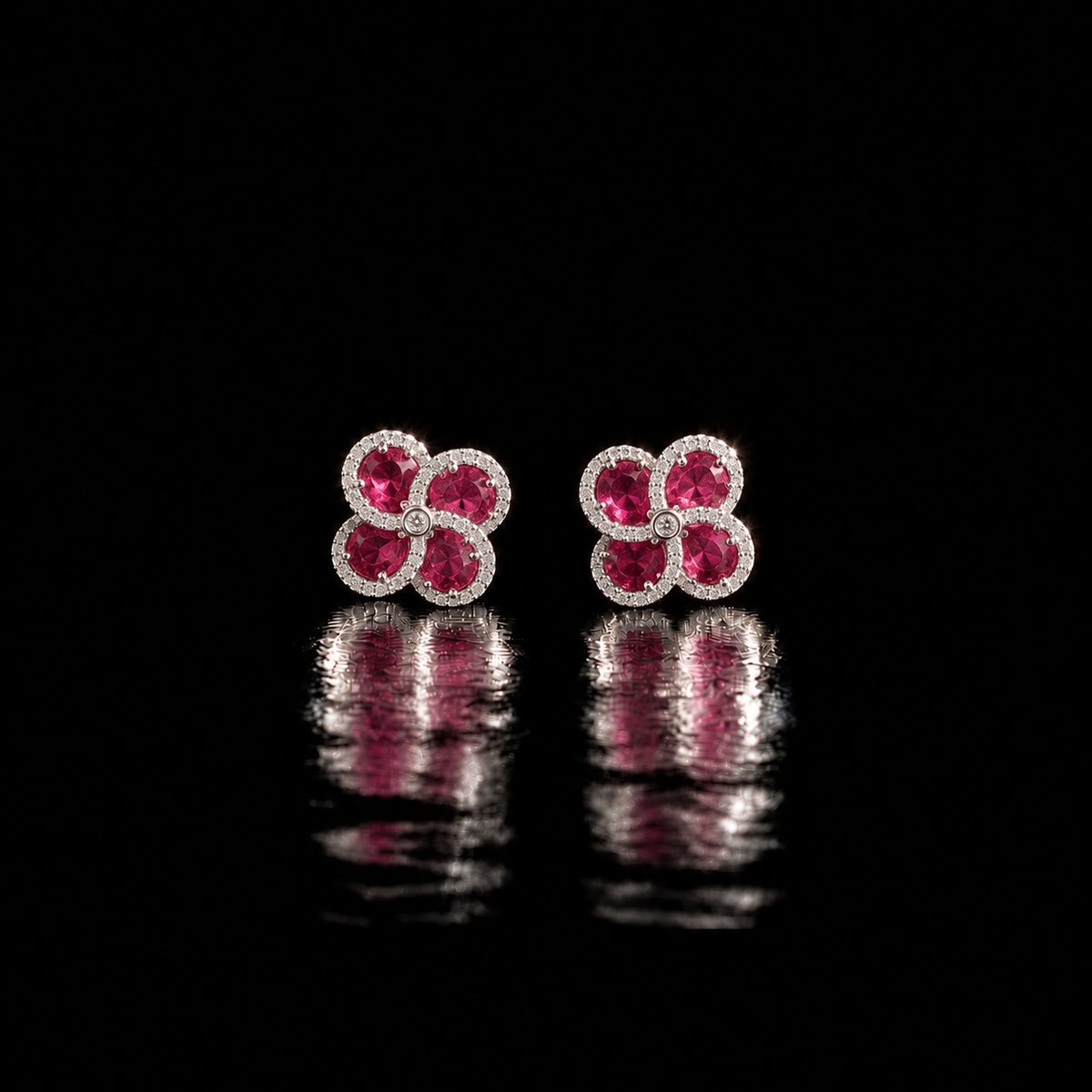 Quadra Halo Stud Earrings with four faceted  ruby pink stones, clear zircon borders and silver-tone setting displayed on a glossy black reflective surface.