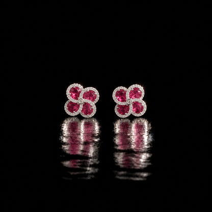 Quadra Halo Stud Earrings with four faceted  ruby pink stones, clear zircon borders and silver-tone setting displayed on a glossy black reflective surface.