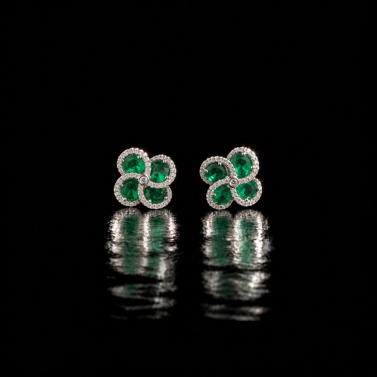 Quadra Halo Stud Earrings with four faceted emerald green stones, clear zircon borders and silver-tone setting displayed on a glossy black reflective surface.