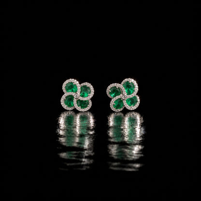 Quadra Halo Stud Earrings with four faceted emerald green stones, clear zircon borders and silver-tone setting displayed on a glossy black reflective surface.