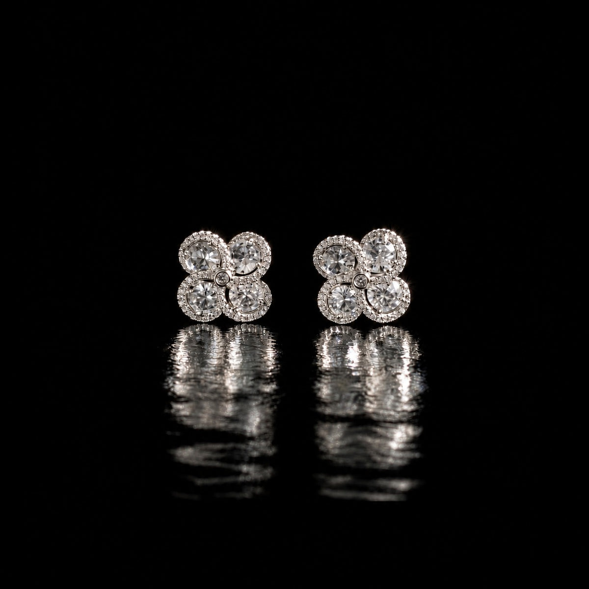 Quadra Halo Stud Earrings with four faceted clear stones, clear zircon borders and silver-tone setting displayed on a glossy black reflective surface.