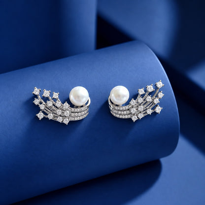 Silver-tone statement earrings with white pearls, curved rows of clear zircon stones and branching crystal details displayed on a blue surface
