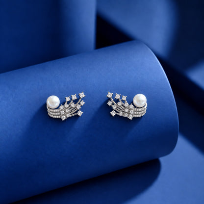 Silver-tone statement earrings with white pearls, curved rows of clear zircon stones and branching crystal details displayed on a blue surface