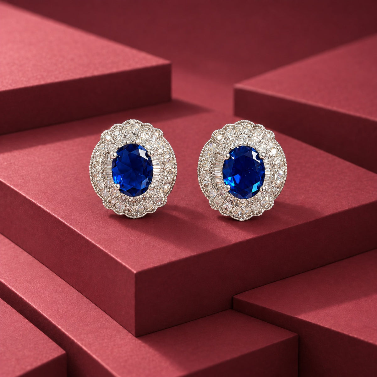 Verdanza Oval statement stud earrings with a faceted oval Sapphire blue centre stone and detailed clear zircon surround in a polished silver-tone setting