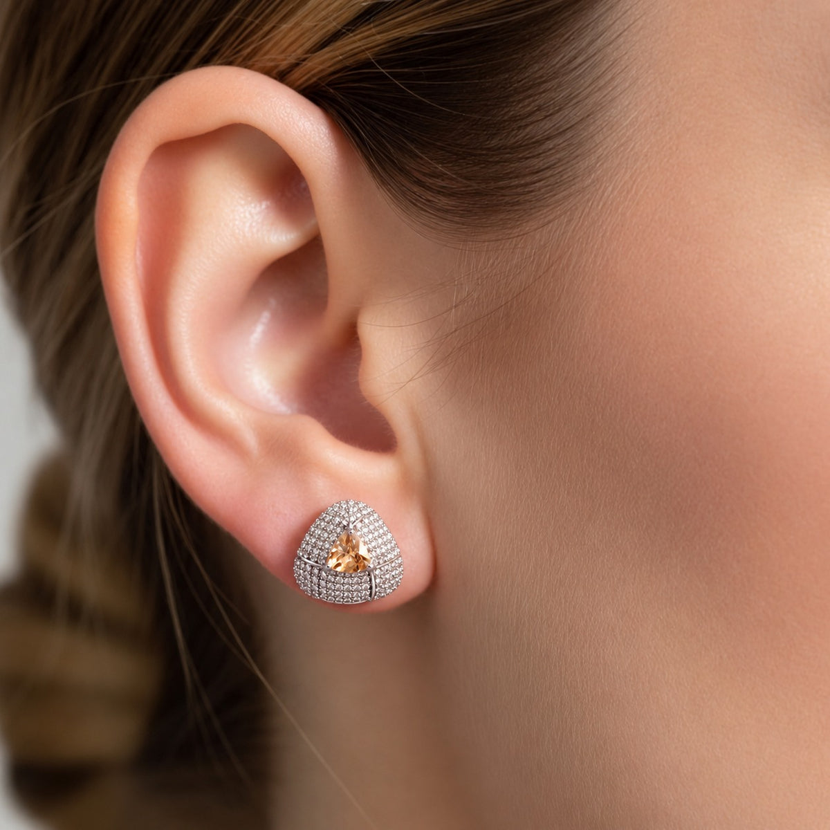 Close-up ear view wearing a triangular coloured stone stud with sparkling clear zircon detailing and a polished silver-tone finish.