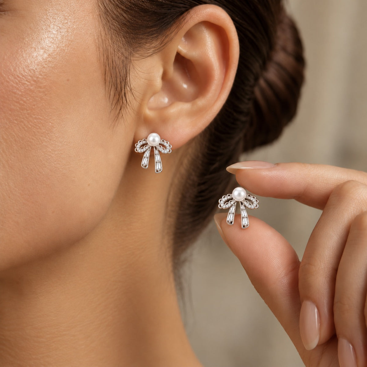 Close-up of silver bow earrings with white pearls and clear zircon stones worn on the ear.