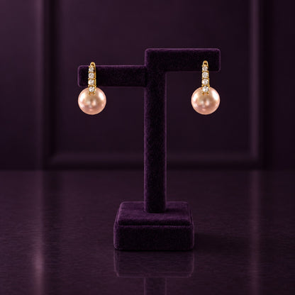 Gold-tone drop earrings with four clear stones and large blush-pink pearl drops displayed on a deep plum jewellery 