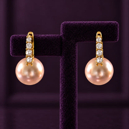 Gold-tone drop earrings with four clear stones and large blush-pink pearl drops displayed on a deep plum jewellery stand.