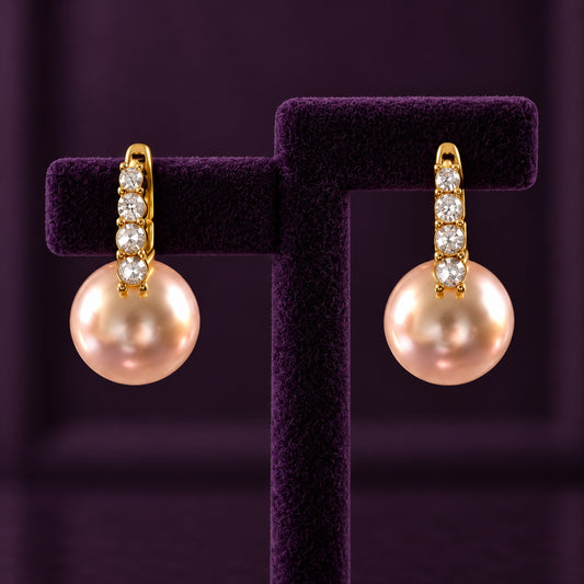 Gold-tone drop earrings with four clear stones and large blush-pink pearl drops displayed on a deep plum jewellery stand.