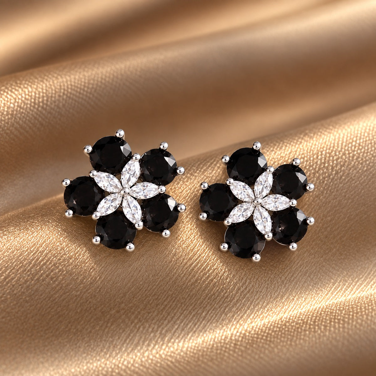 Pair of Fivefold Bloom Studs featuring five faceted black stones surrounding a clear marquise-cut crystal flower in a polished silver-tone setting, displayed on beige satin.