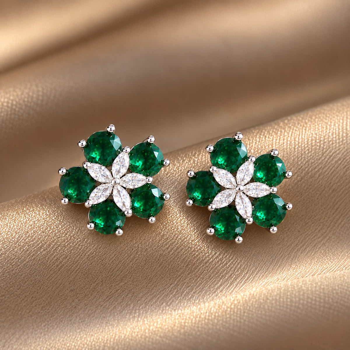 Pair of Fivefold Bloom Studs featuring five faceted  emerald green stones surrounding a clear marquise-cut crystal flower in a polished silver-tone setting, displayed on beige satin.