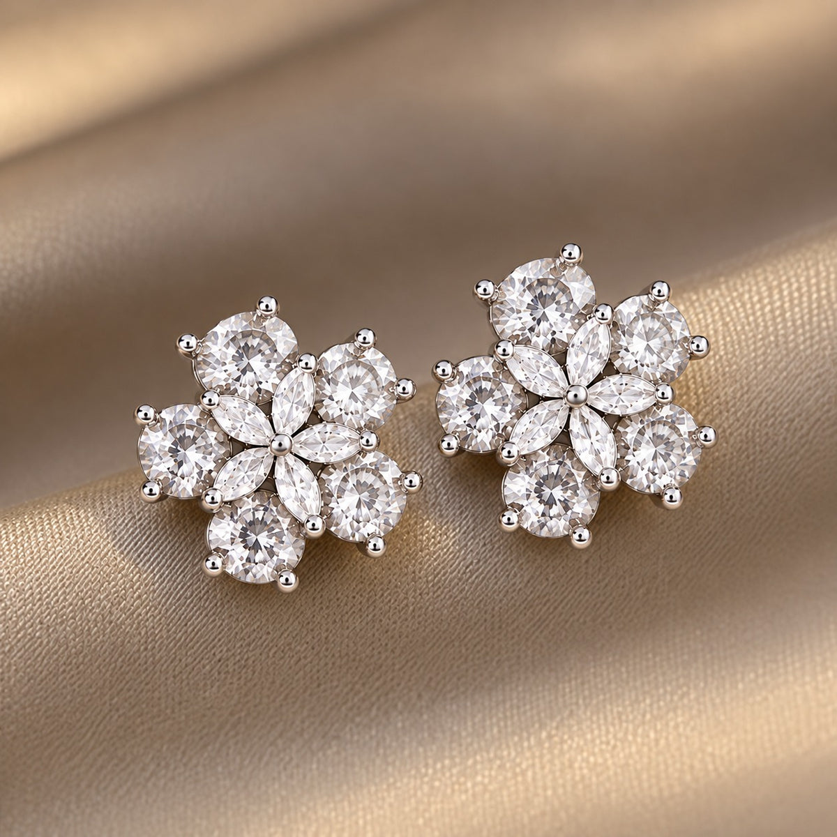 Pair of Fivefold Bloom Studs featuring five faceted clear stones surrounding a clear marquise-cut crystal flower in a polished silver-tone setting, displayed on beige satin.