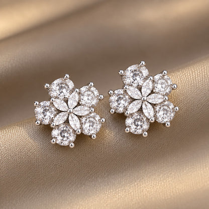 Pair of Fivefold Bloom Studs featuring five faceted clear stones surrounding a clear marquise-cut crystal flower in a polished silver-tone setting, displayed on beige satin.