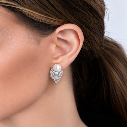 Close-up of a woman wearing Pearl Cascade Studs, featuring a round white pearl above layered silver-tone rows of clear zircon that taper below the earlobe.