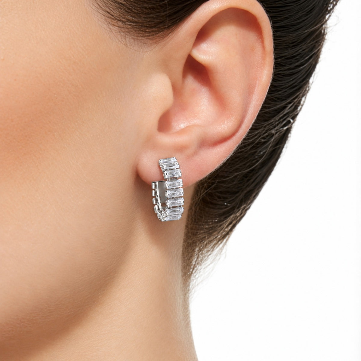 Close-up of a woman wearing the silver Linear Arc Hoop, featuring a curved row of rectangular clear zircon stones framing the earlobe