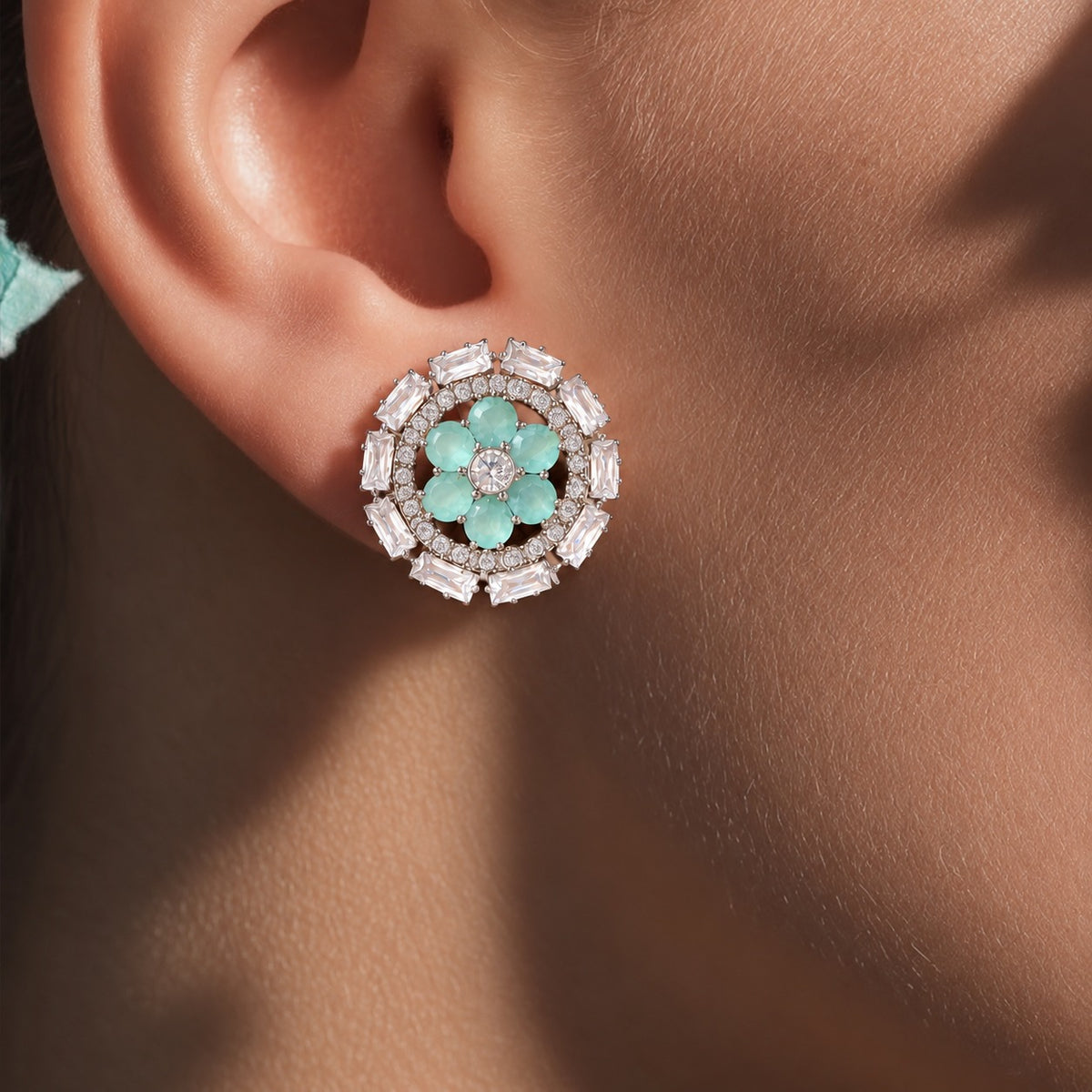 Close-up of aqua blue Petal Orbit Stud Earring worn on the ear, featuring six gemstone petals surrounded by clear round zircon and rectangular clear stones.