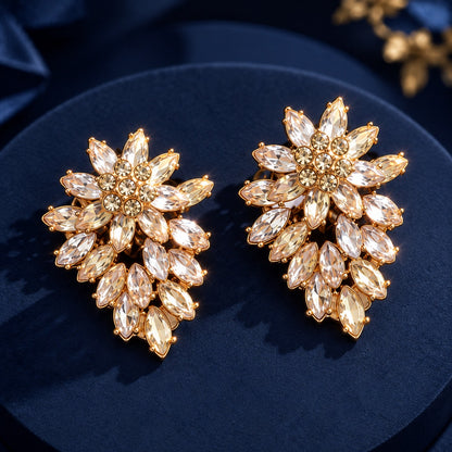 Close-up of Gilded Laurel Drop Earrings in gold-tone metal, featuring layered marquise-cut clear stones arranged in a floral tapered design on deep navy fabric