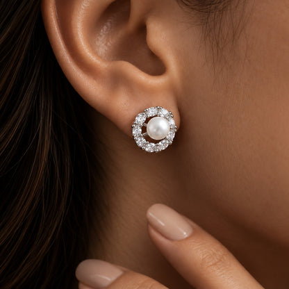 Close-up of a woman wearing a Pearl Circuit Stud Earring with a white pearl centre framed by a circular arrangement of clear stones in silver-tone metal