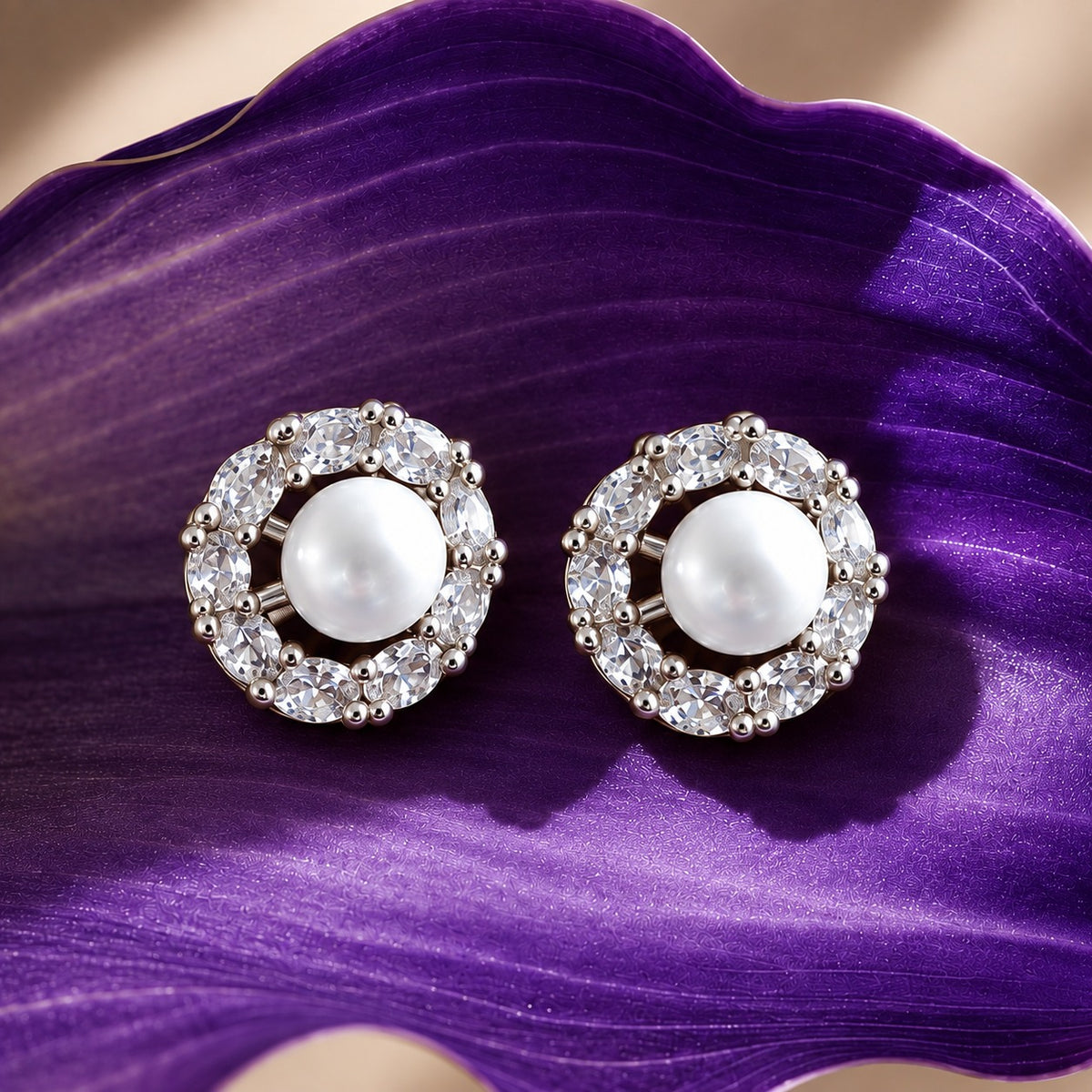 Pearl Circuit silver-tone stud earrings featuring round white pearl centres surrounded by a circular frame of clear faceted stones on a deep purple surfac