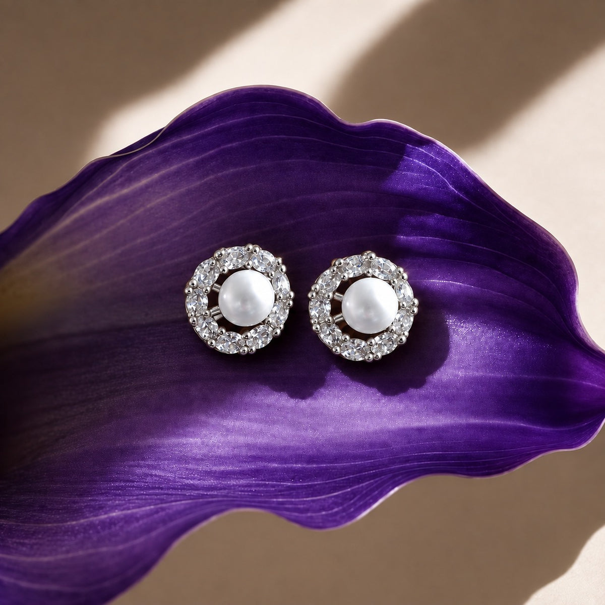 Pearl Circuit silver-tone stud earrings featuring round white pearl centres surrounded by a circular frame of clear faceted stones on a deep purple surfac