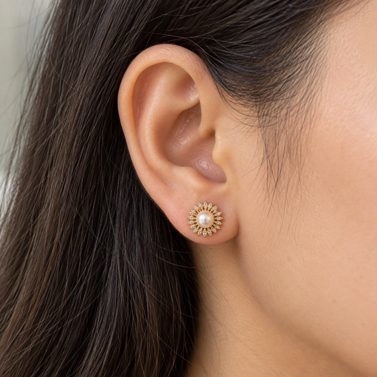 Woman wearing a compact gold-tone Pearl Sunray Stud Earring with a central white pearl and symmetrical ring of clear marquise stones.