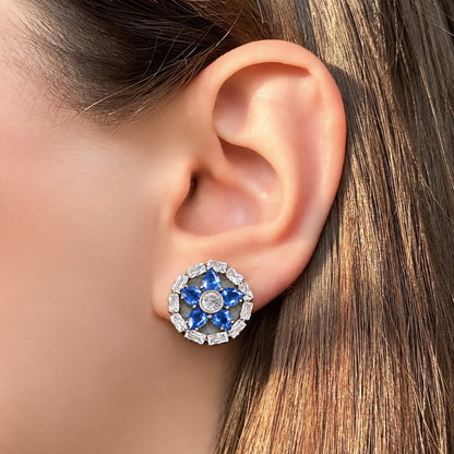 Close-up of a woman wearing Petal Circuit Stud Earrings with blue pear-cut gemstone petals, a clear zircon centre and geometric baguette-stone border.