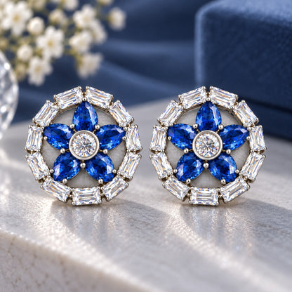 Petal Circuit Stud Earrings featuring five  sapphire blue pear-cut coloured gemstone petals, a round clear zircon centre and a circular border of clear baguette stones in silver-tone metal.”