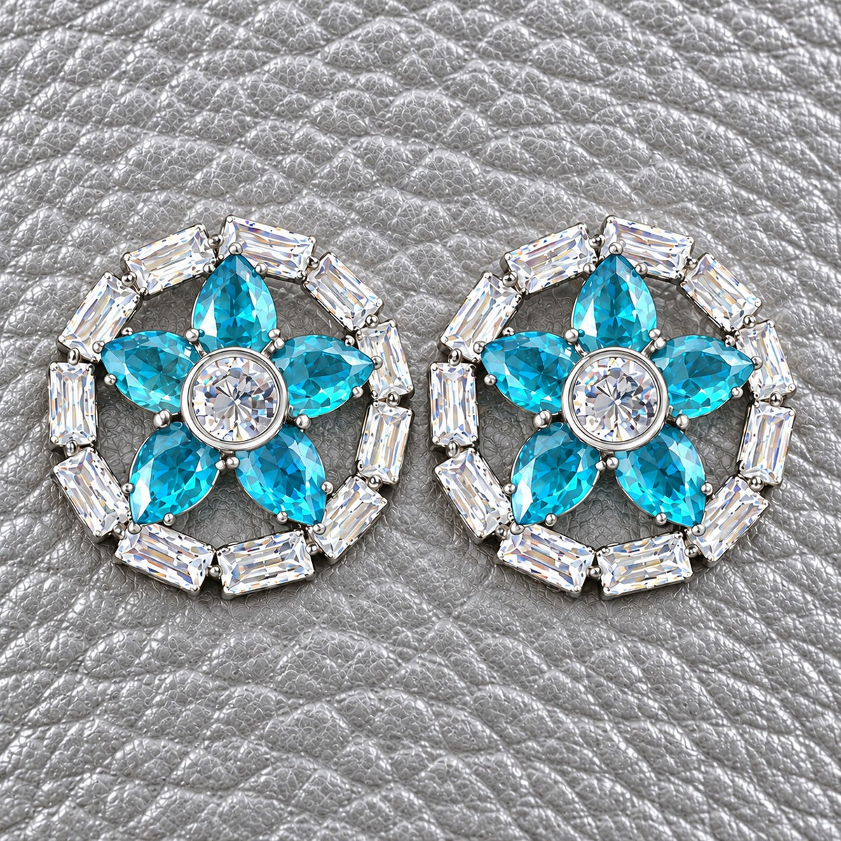 Petal Circuit Stud Earrings featuring five  aqua blue pear-cut coloured gemstone petals, a round clear zircon centre and a circular border of clear baguette stones in silver-tone metal.”
