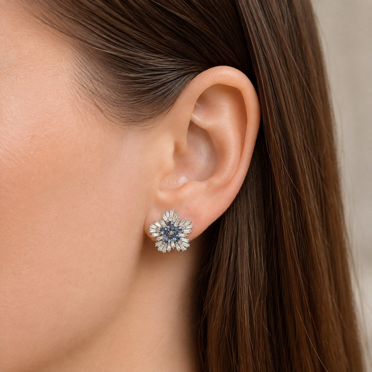 Woman wearing Sapphire Fan Stud Earrings with deep blue pear-cut stones and a sculpted border of clear baguette stones in silver-tone meta