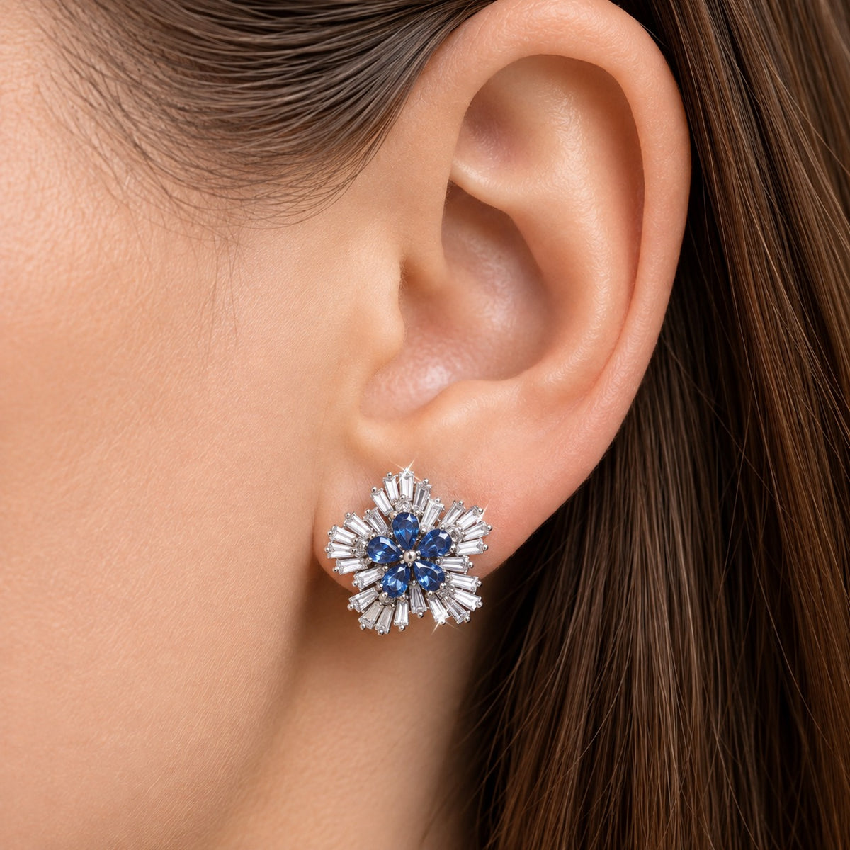 Woman wearing Sapphire Fan Stud Earrings with deep blue pear-cut stones and a sculpted border of clear baguette stones in silver-tone metal