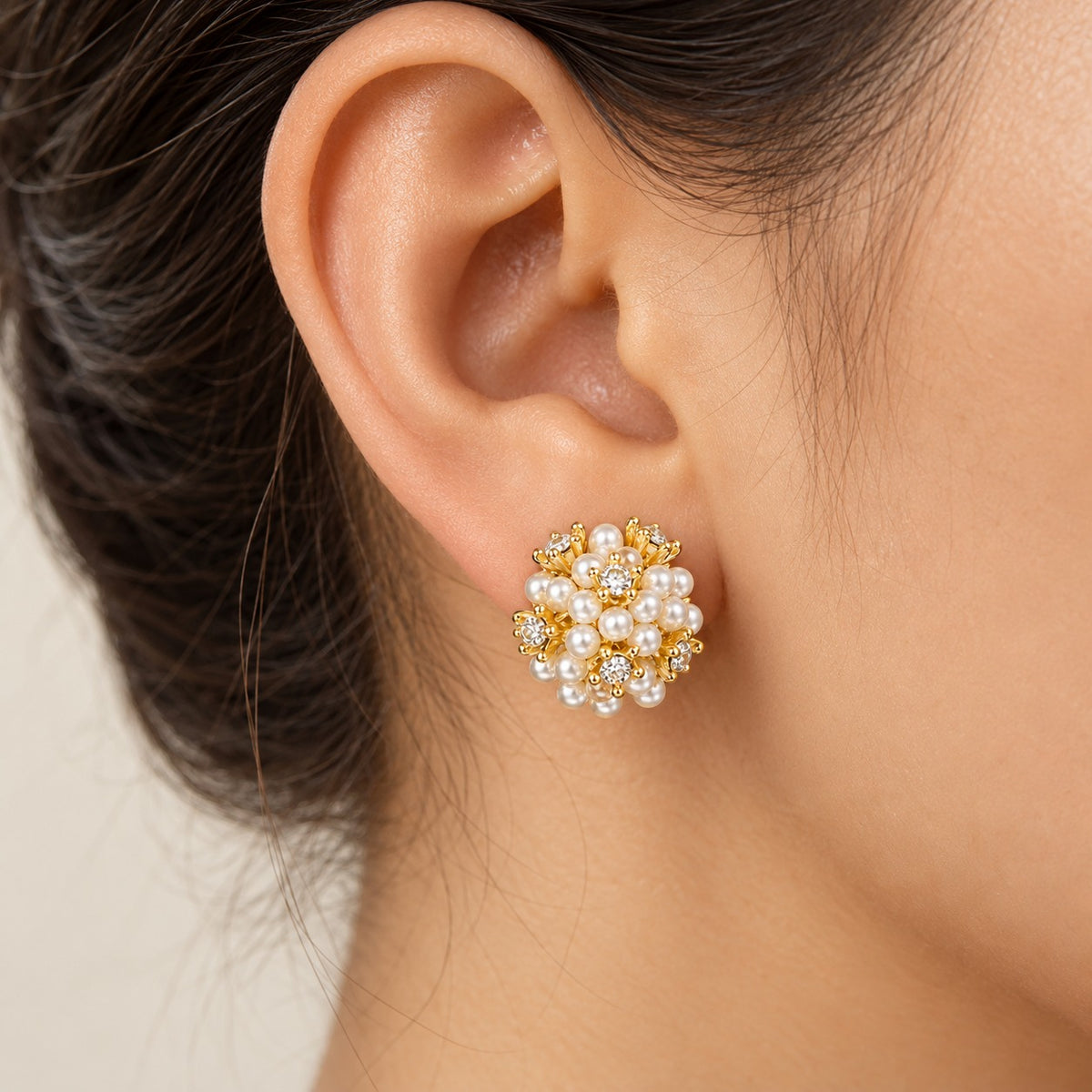 Pearl Riot Stud Earring worn on the ear, showing its rounded dimensional cluster of ivory pearls, clear zircon accents and polished gold-tone setting
