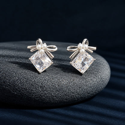 Close-up of Bowline Quartz Stud Earrings with clear diamond-shaped zircon stones, three white pearls and polished silver-tone bow detailing.