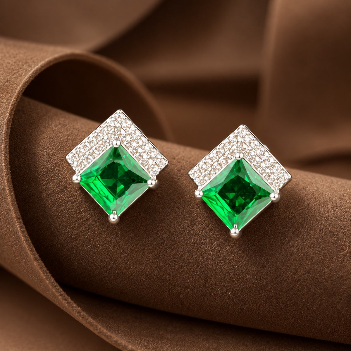 Pair of geometric silver-tone stud earrings with square-cut coloured gemstones and clear zircon detailing displayed on a sculptural brown jewellery stand.