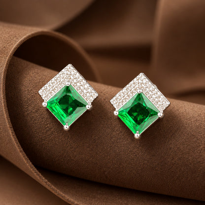Pair of geometric silver-tone stud earrings with square-cut coloured gemstones and clear zircon detailing displayed on a sculptural brown jewellery stand.