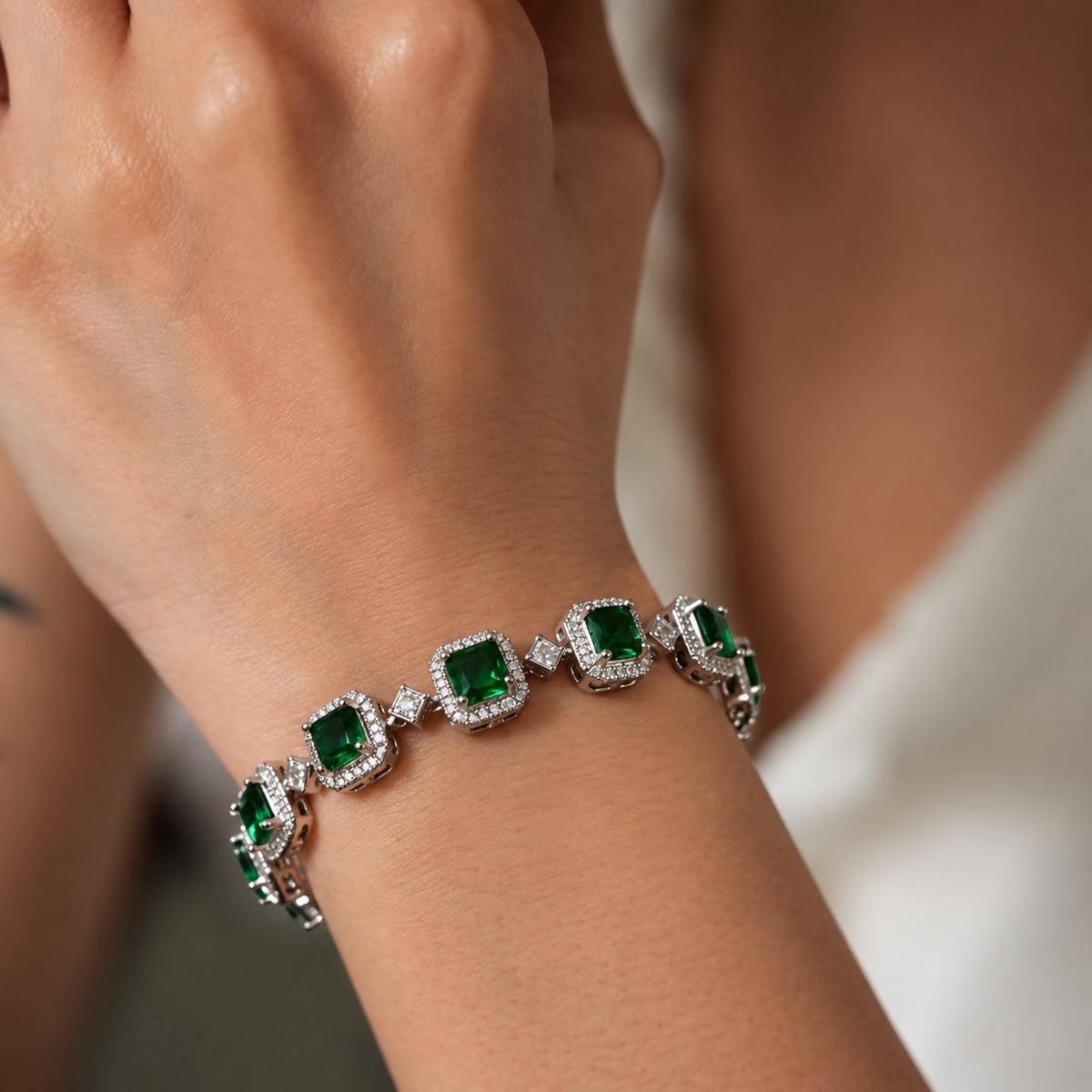 Close-up of the Regal Grid Bracelet worn around the wrist, featuring square-cut green gemstones in a silver-tone zircon setting with geometric connecting links.