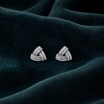 Vela Fold S925 sterling silver stud earrings with interwoven triangular bands and clear zircon stones displayed on deep teal fabric.