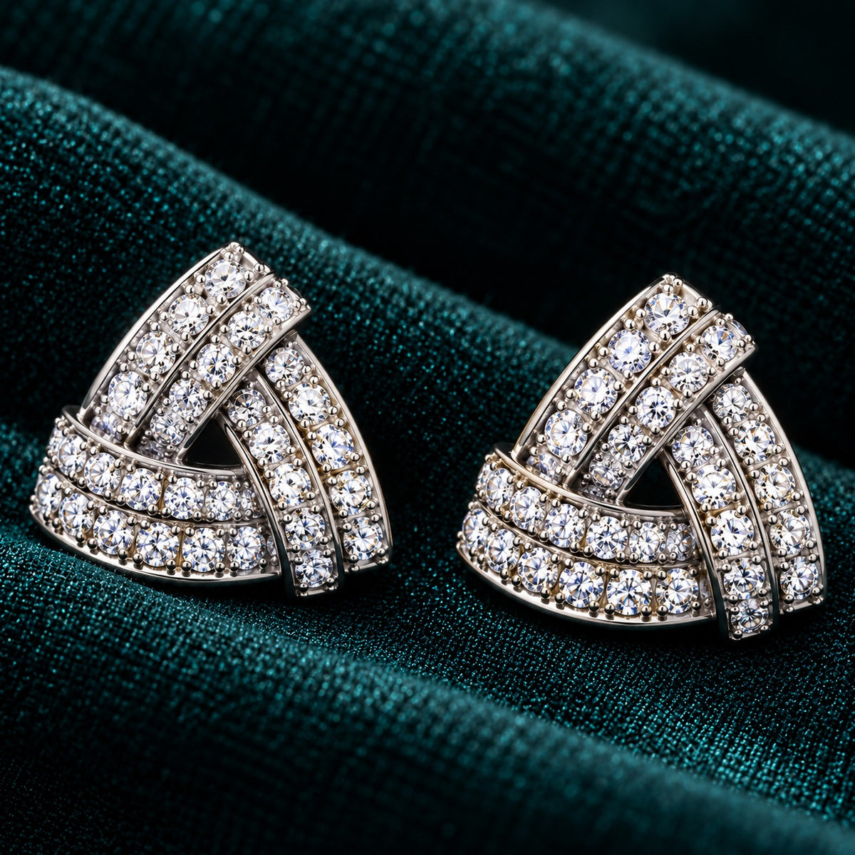 Vela Fold S925 sterling silver stud earrings with interwoven triangular bands and clear zircon stones displayed on deep teal fabric.