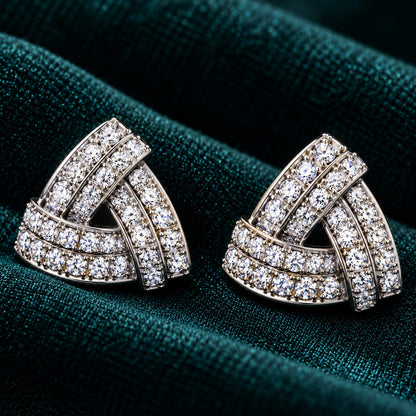 Vela Fold S925 sterling silver stud earrings with interwoven triangular bands and clear zircon stones displayed on deep teal fabric.