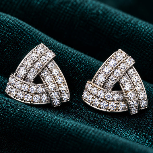 Vela Fold S925 sterling silver stud earrings with interwoven triangular bands and clear zircon stones displayed on deep teal fabric.