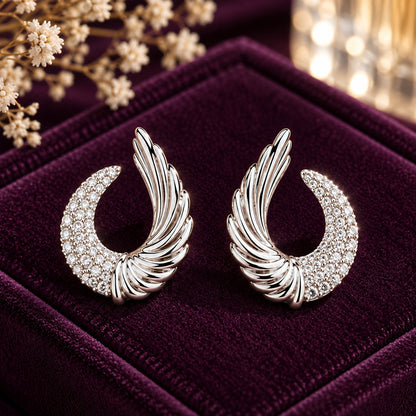 Celestial Wing Crescent Studs in polished silver with clear zircon stones displayed on a deep plum velvet jewellery box.