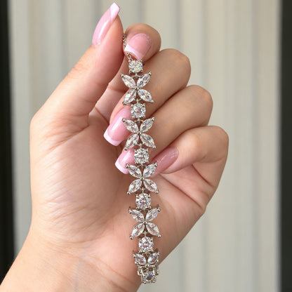 Close-up of silver-tone bracelet featuring four-petal marquise zircon flowers alternating with round clear zircon stones held in hand.