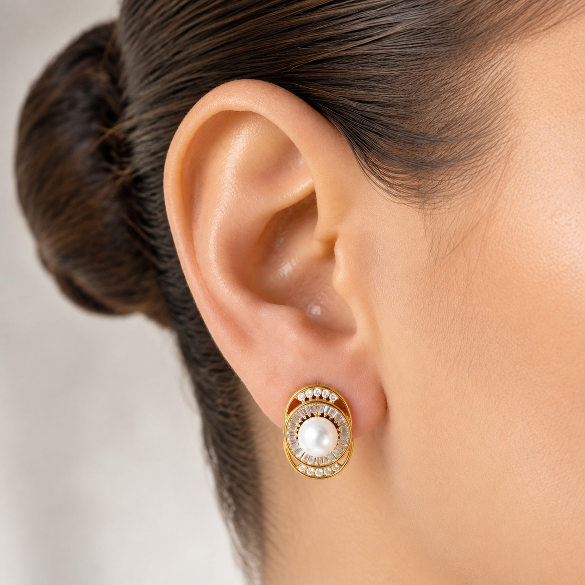 Pearl Meridian gold-tone stud earring worn on the ear, featuring a white pearl centre framed by baguette and round clear zircons