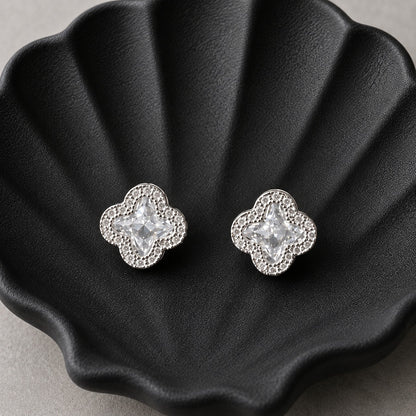 S925 sterling silver quatrefoil stud earrings with faceted clear centre crystals and zircon borders displayed on a black shell-shaped tray.