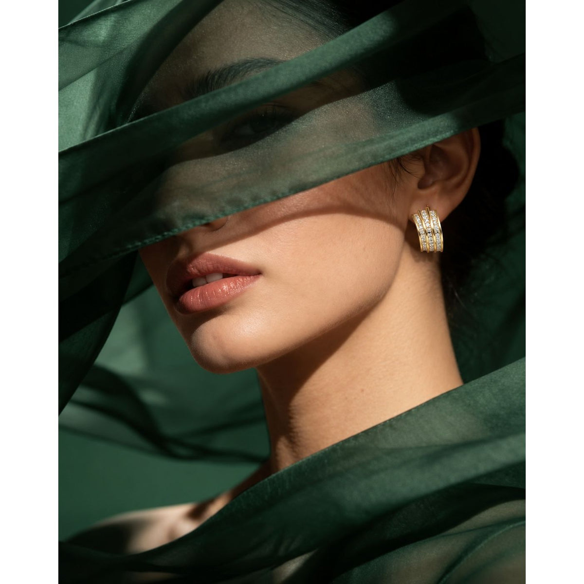 Model wearing Gilded Trio Arc Hoops featuring three gold curved bands accented with rows of clear zircons.